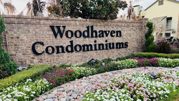 A sign for Woodhaven Condominiums with a landscaped garden featuring various plants and a stone pathway. - Momo's sweet home 2BR/2BA (Dallas)