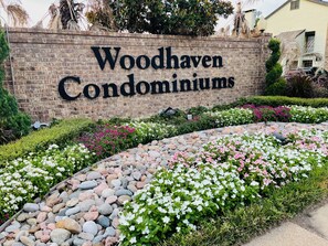 A sign for Woodhaven Condominiums with a landscaped garden featuring various plants and a stone pathway.