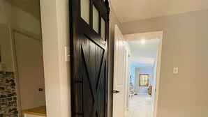 A hallway with a dark wooden door, white walls, and a tiled floor. - Momo's sweet home 2BR/2BA (Dallas)