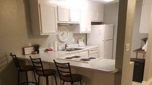 A kitchen with white cabinets, a clock, and a bar area with stools. - 6 beds, 3 bedrooms, grill, small backyard and firepit, close to beach (Fort Walton Beach)
