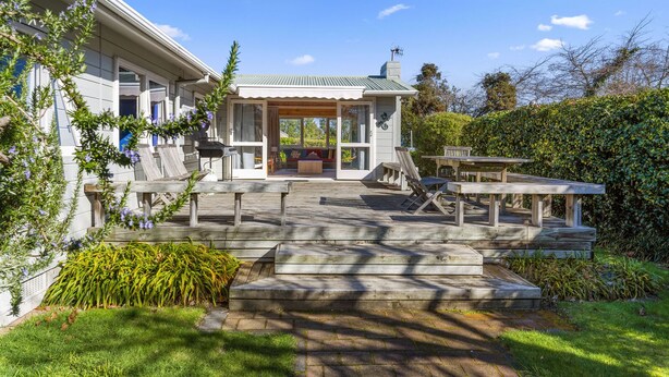 Ein Haus mit überdachter Terrasse, Sitzgelegenheiten im Freien und einem gepflegten Garten.