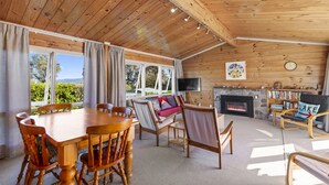 Ein geräumiger Wohnbereich mit Holzboden, Kamin, Fernseher und einem Esstisch mit Stühlen.
