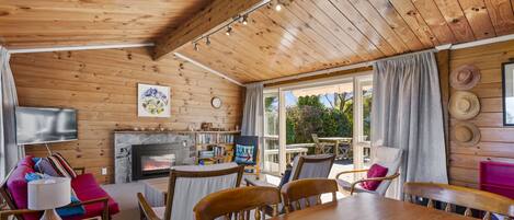 Un interior de cabaña acogedor, con techo de madera, chimenea, comedor y vistas al exterior.