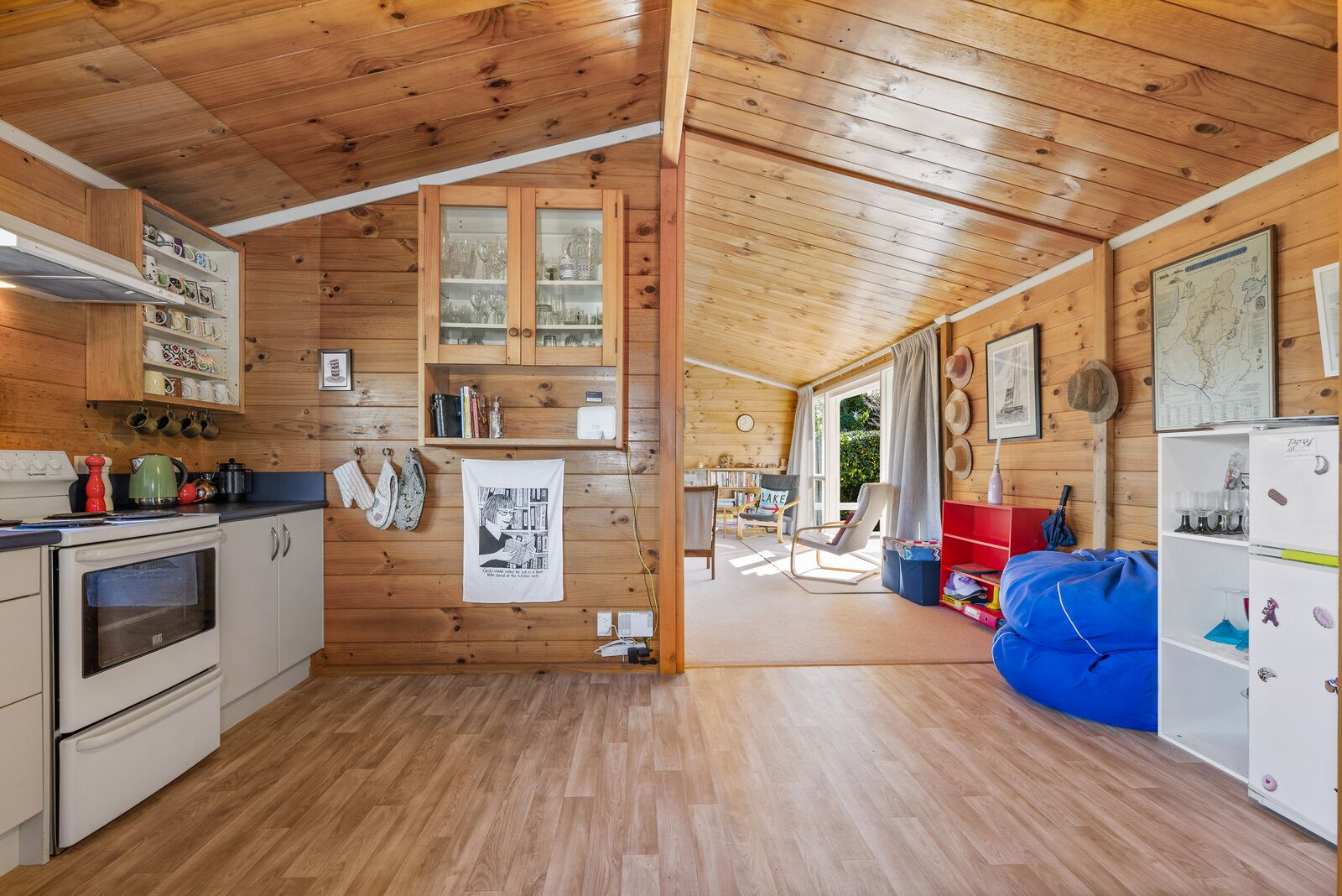 Ambiente interno in legno con cucina, zona pranzo e soggiorno con pouf blu.