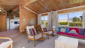 Ein gemütliches Blockhauss-Interieur mit Holzwänden, einem Essbereich mit Stühlen und Tisch, einer Couch mit Kissen und einer Küchenzeile mit Geräten.