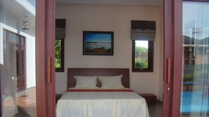 Une chambre avec un grand lit, deux tables de chevet, un tableau au mur et une vue sur une piscine, visible à travers une porte vitrée.