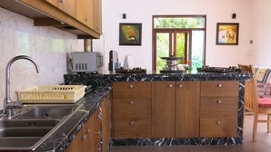 Une cuisine dotée d’un plan de travail en marbre, de meubles en bois, d’un évier et d’une fenêtre donnant sur un paysage verdoyant.