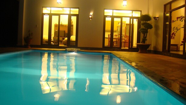 Une piscine à l’eau claire, entourée d’un bâtiment doté de grandes portes et fenêtres en verre, et dont l’intérieur, bien éclairé, est visible à travers ces portes.