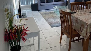 Een moderne woonkamer met een grijze bank, een eettafel met stoelen, een witte salontafel en een boekenkast.