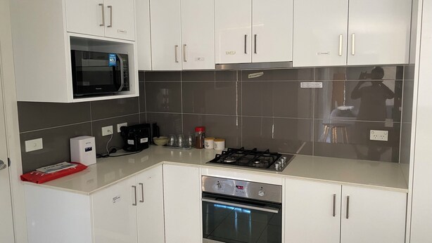 Een moderne keuken met witte kastjes, een magnetron, een koffiezetapparaat, een gasfornuis en een oven.