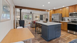 A modern kitchen with wooden cabinets, a central island, stainless steel appliances, and a dining area with a wooden table and chairs. - Walk to Village, Sharc Passes, Air Conditioning, King Bed, Bikes (Sunriver)