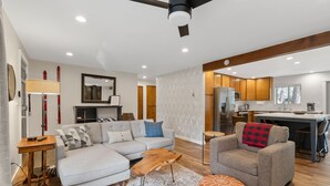 A modern living room with a sofa, ottoman, and coffee table, connected to a kitchen area with wooden cabinets and a dining table. - Walk to Village, Sharc Passes, Air Conditioning, King Bed, Bikes (Sunriver)