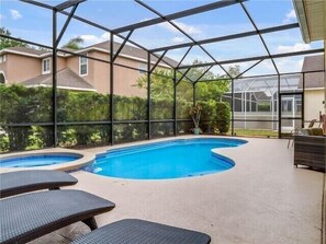 A covered swimming pool with two lounge chairs and a table, surrounded by a metal frame and glass panels.