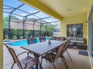 A sunlit patio with a pool, a dining table, and a sofa.