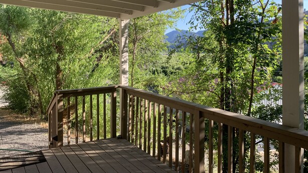 Eine Holzterrasse mit Geländer, umgeben von Bäumen und einem Berg im Hintergrund.