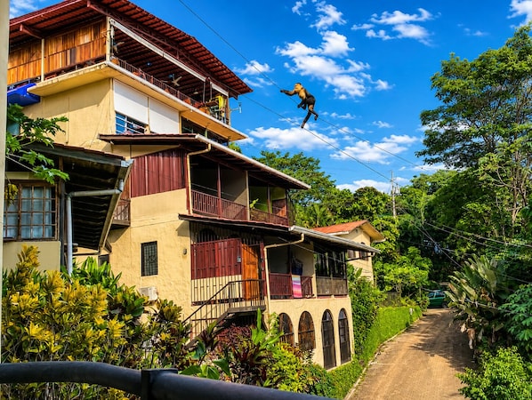 A multi-story building with balconies, a dirt road, and lush greenery.