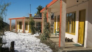 A building with a red roof and white walls, featuring a covered outdoor area with a bench and a small table.