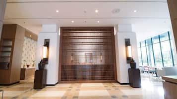 A modern lobby with a reception desk, a wooden slat partition, and a seating area with tables and chairs.