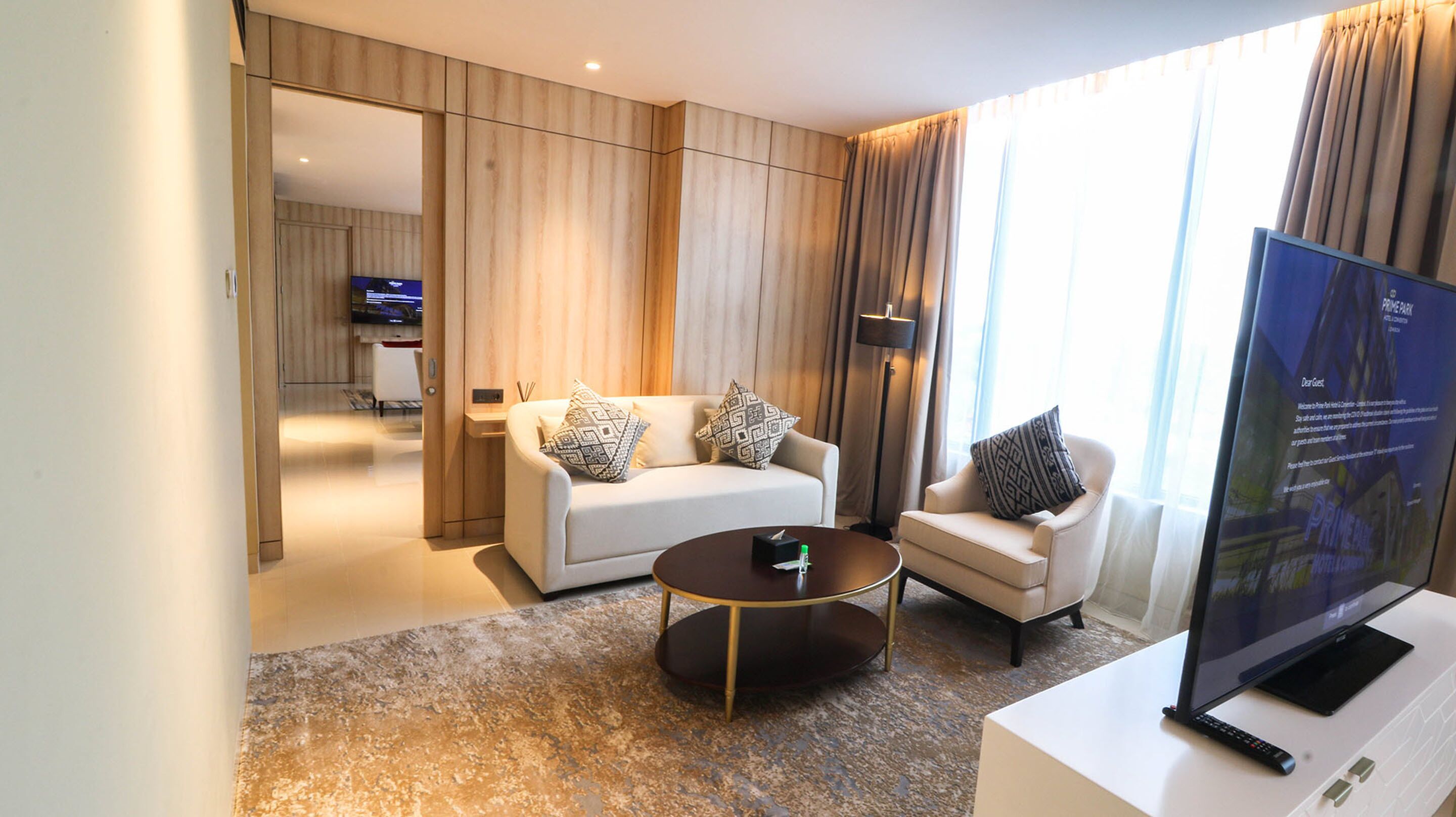 Quarto de hotel moderno com sofá, poltrona e televisão de tela plana.