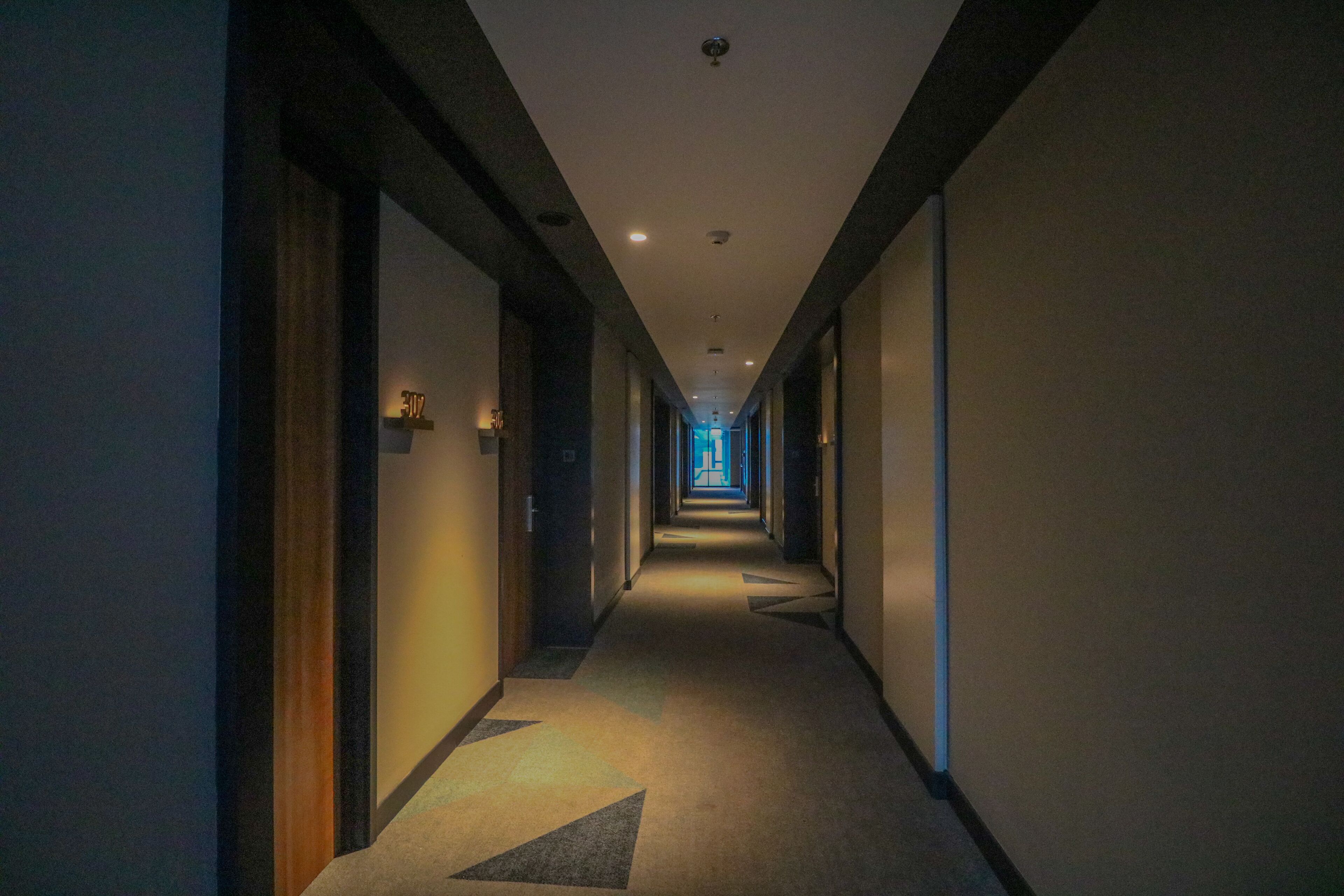 A long, narrow hotel corridor with doors on both sides, leading to rooms.