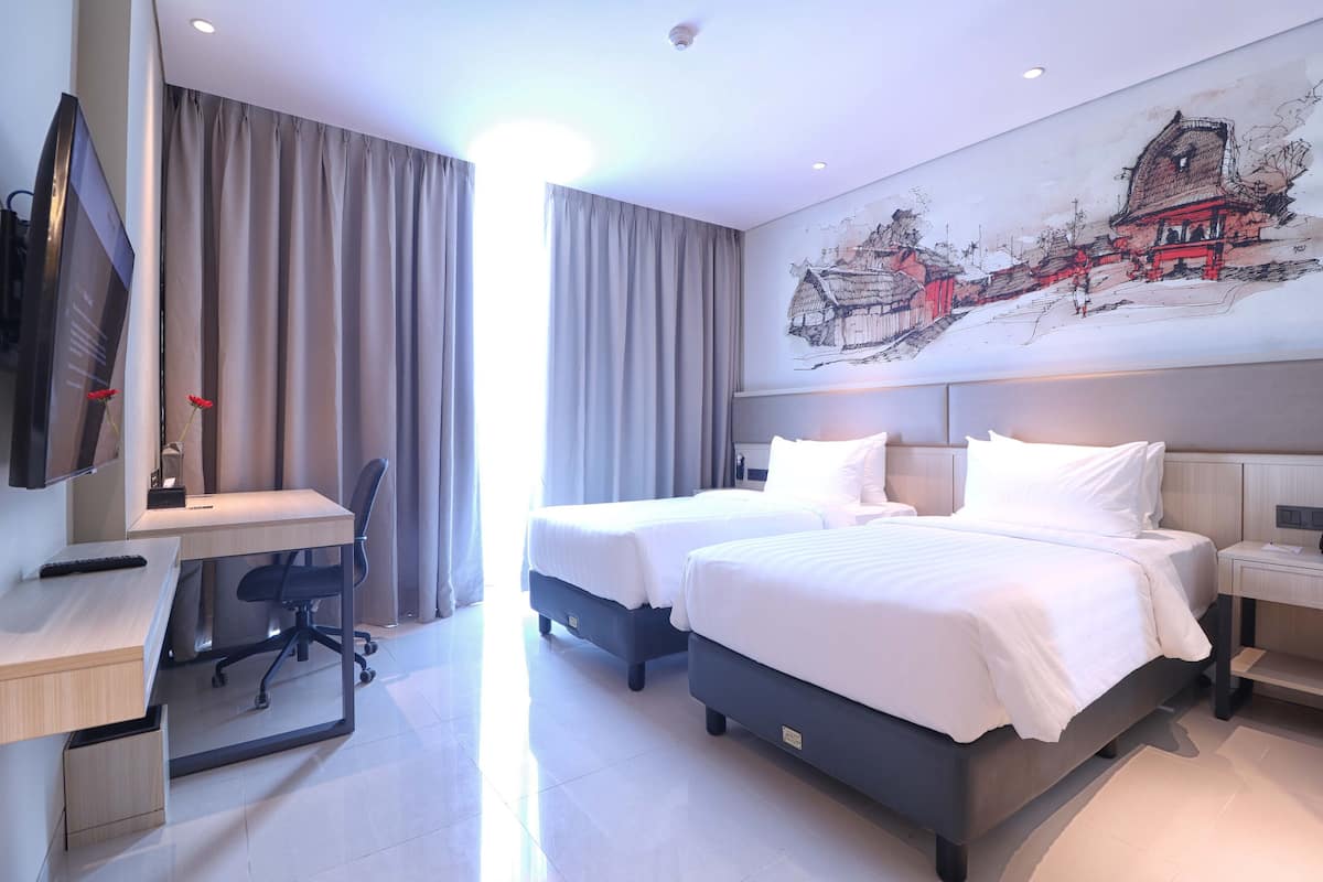 A hotel room with two beds, a desk, a chair, a TV, and a painting on the wall.