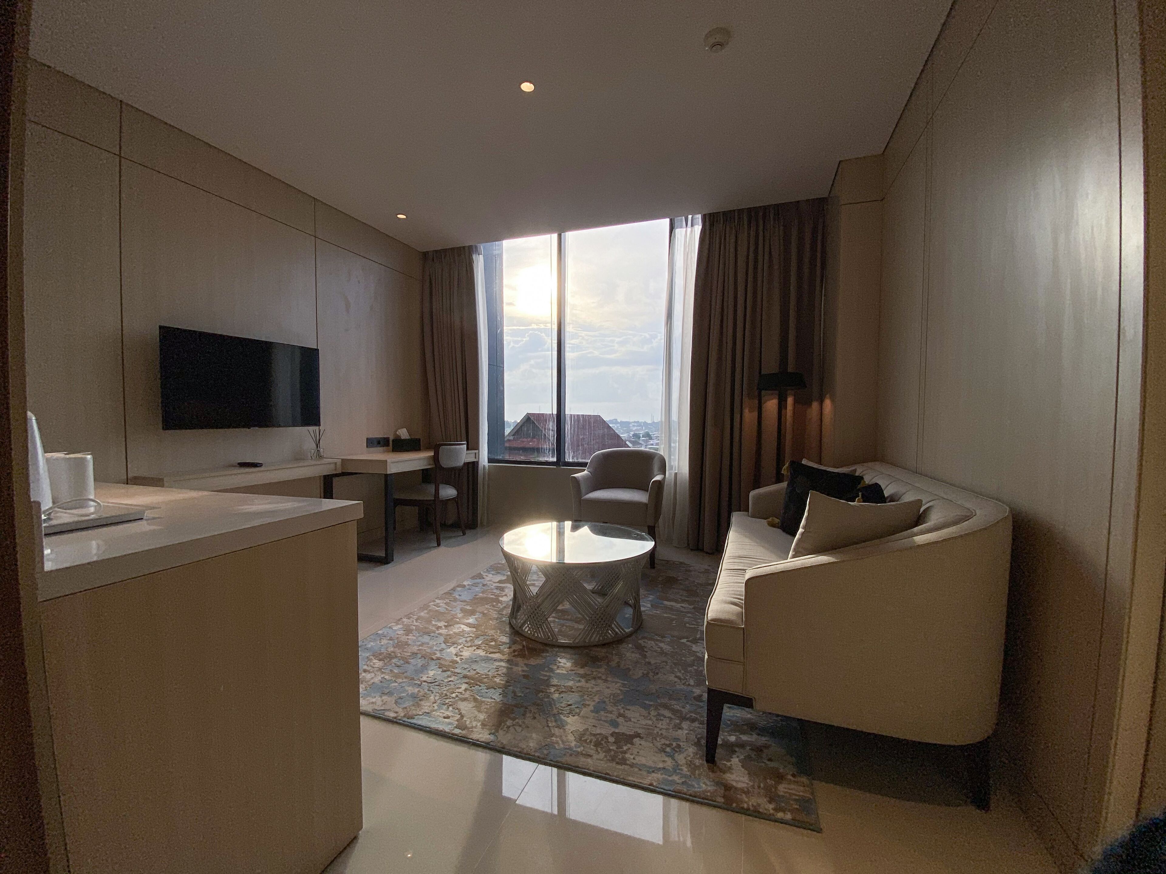Een moderne hotelkamer met een flatscreen-tv, een bank, een eettafel en een groot raam met uitzicht op de stad.