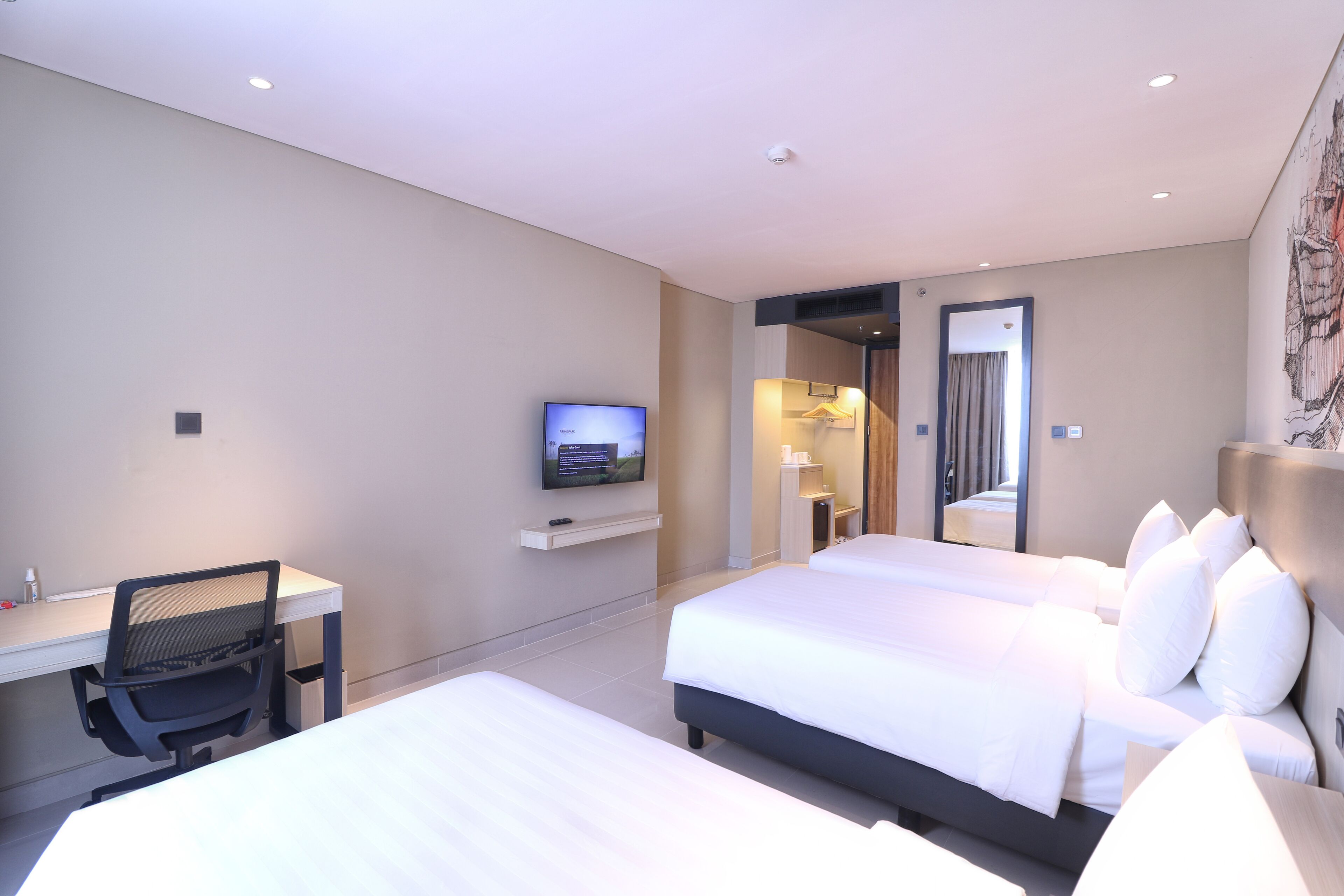 A hotel room with two beds, a desk, a TV, and a bathroom visible through an open door.