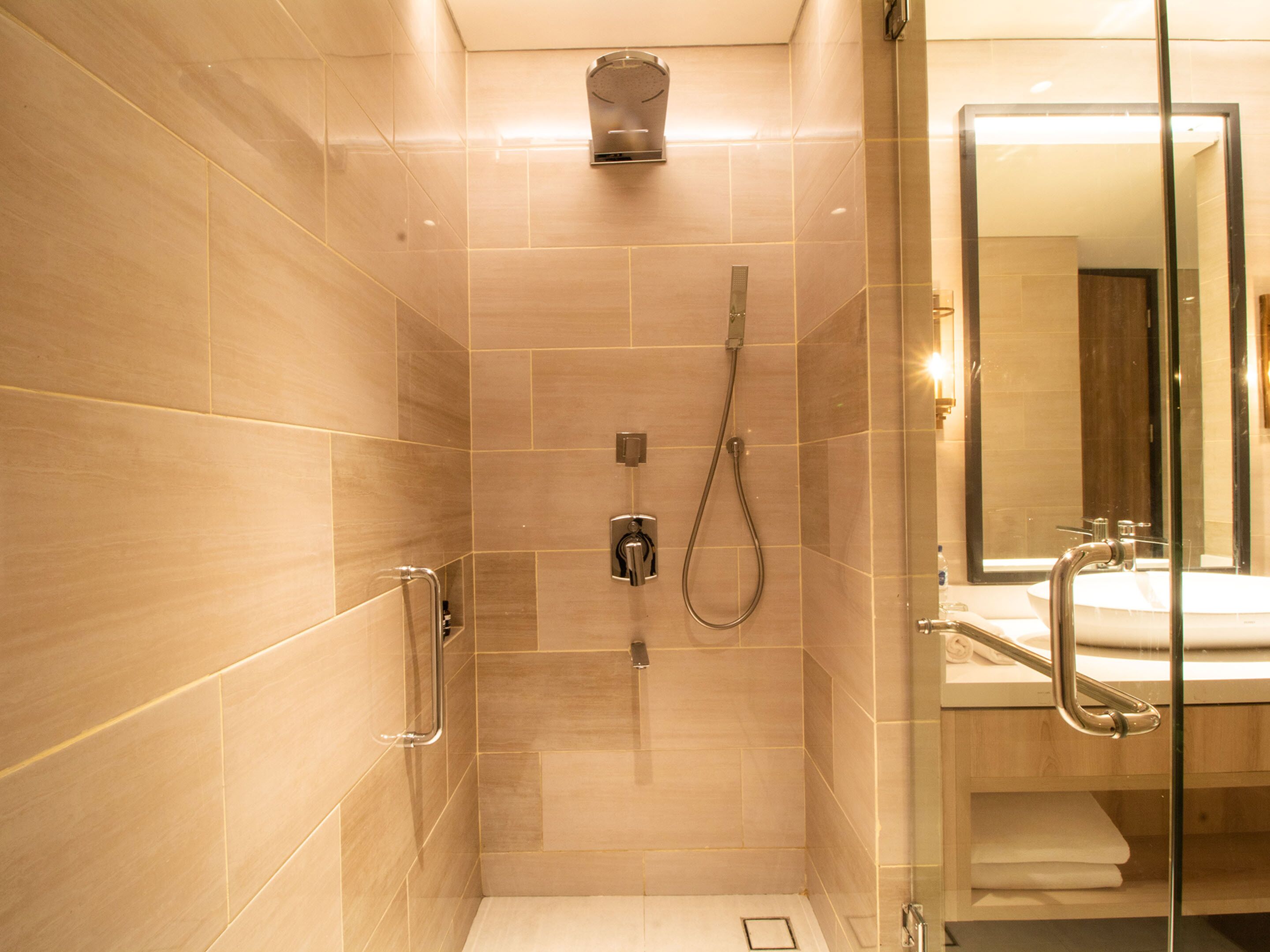 Ein modernes Badezimmer mit Duschkabine aus Glas, Handlauf und Waschbecken mit Spiegel.