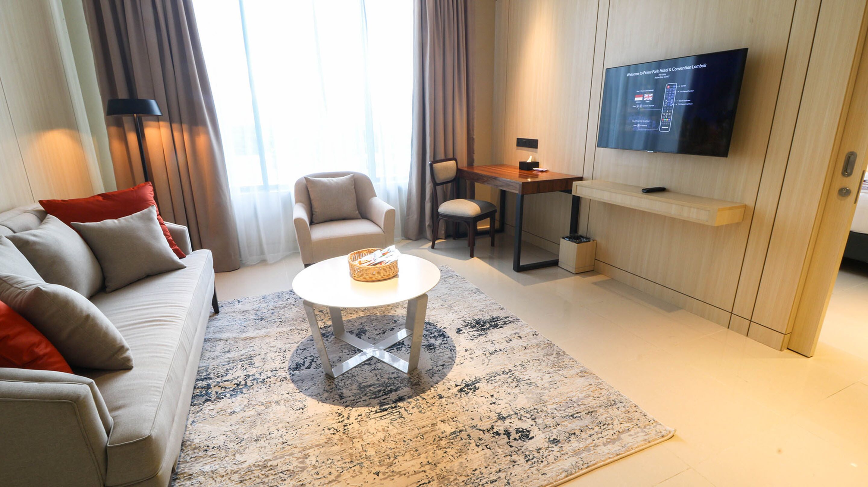 A modern living room with a sofa, armchair, coffee table, and a flat-screen TV mounted on the wall.