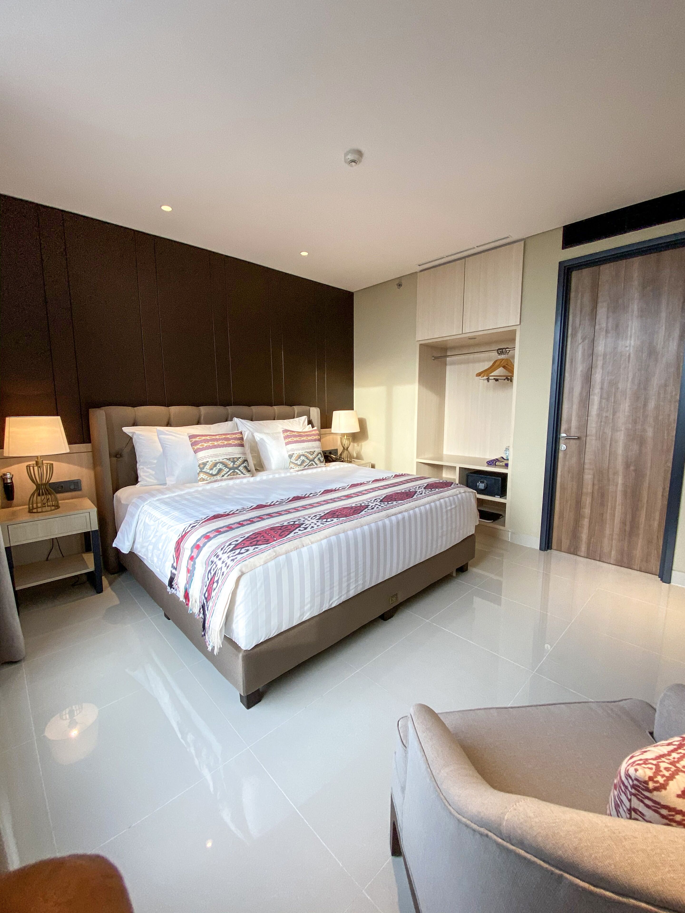 A modern bedroom with a large bed, bedside tables, a wardrobe, and a seating area.