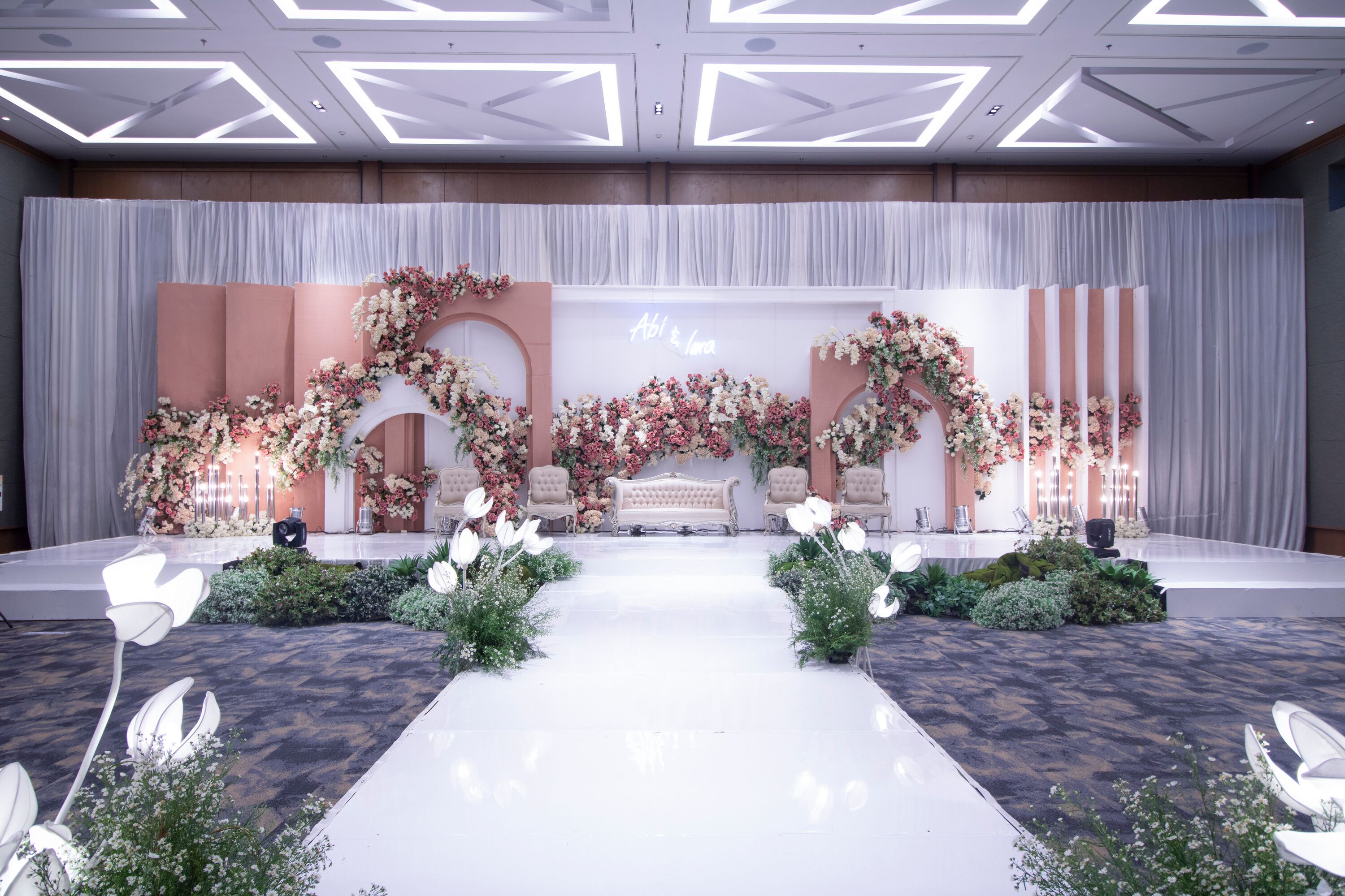 A stage with floral decorations, a white backdrop, and a bench.