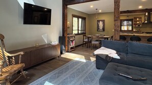 A living room with a sofa, a television, a dining area with chairs, and a kitchen in the background. - Mt Baker Luxury Cabin • 2 King Beds • Hot Tub • Game Loft • Firepit (Deming)