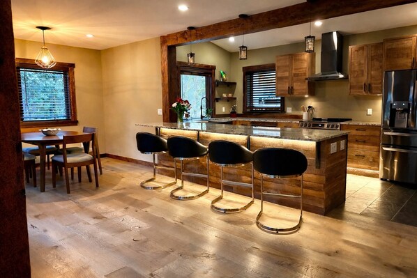 Una cocina moderna con una isla central, taburetes de bar, armarios de madera y electrodomésticos de acero inoxidable.