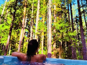Una persona relajándose en un jacuzzi rodeado de altos árboles.