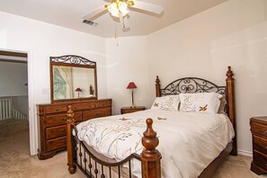 Une chambre à coucher avec un lit en bois, une table de chevet, une commode, un ventilateur de plafond et un miroir.