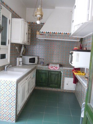 Une cuisine compacte avec des meubles blancs, un four à micro-ondes, un évier et des carreaux décoratifs sur le mur derrière l’évier.