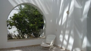 A white chair in a sunlit room with a large arched window overlooking greenery. - House With Garden Wala (El Djem)