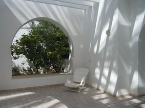 Une chaise blanche dans une pièce baignée de lumière, avec une grande fenêtre en arc donnant sur un paysage verdoyant.