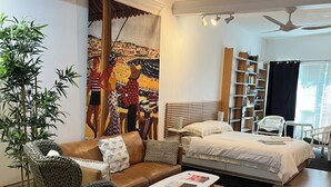 A modern living room with a brown leather sofa, a green woven armchair, a white coffee table, and a large painting on the wall.