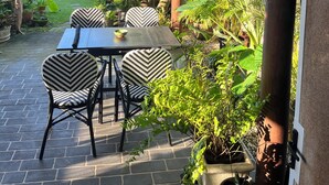 An outdoor patio with a table and chairs, surrounded by potted plants and a view of a residential area.