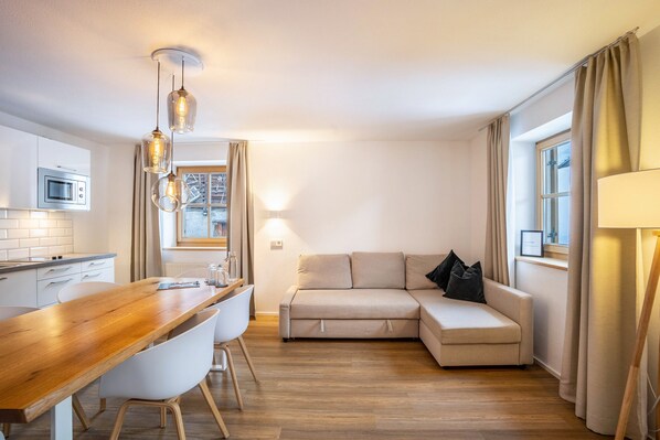 Une cuisine moderne avec un plan de travail en bois, des chaises blanches et des luminaires suspendus.
