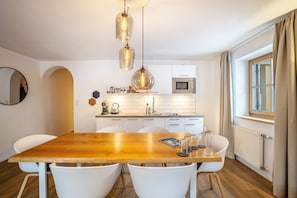 Une cuisine moderne avec des meubles blancs, une table à manger en bois et des luminaires suspendus.
