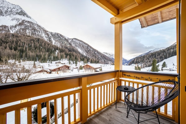 Un balcon en bois offrant une vue sur des montagnes enneigées et des maisons.