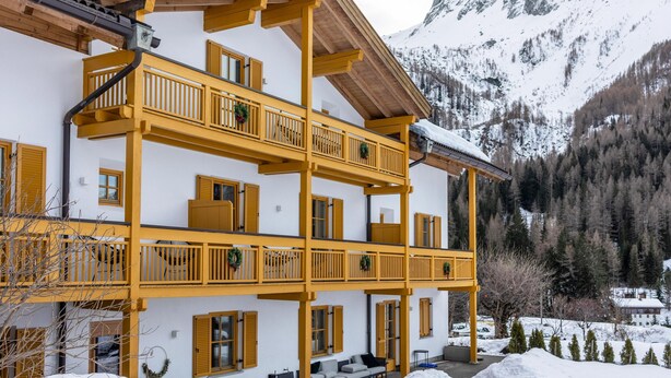Ein mehrstöckiges Gebäude mit Balkonen, Holellenträger und einer Bergkulisse.