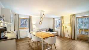 Eine moderne Küche mit Holztisch und Stühlen, einem Essbereich mit einer Couch und großen Fenstern mit Vorhängen.