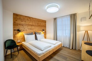 Une chambre avec une tête de lit en bois, un lit avec une literie blanche, un bureau avec une lampe et une chaise.