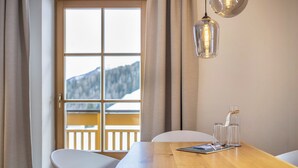 Een eetruimte met een houten tafel, stoelen, een raam met uitzicht op bergen en een hanglamp.