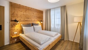 Een kamer met een houten hoofdbord, een bed met witte lakens, een bedlamp en een vloerlamp.