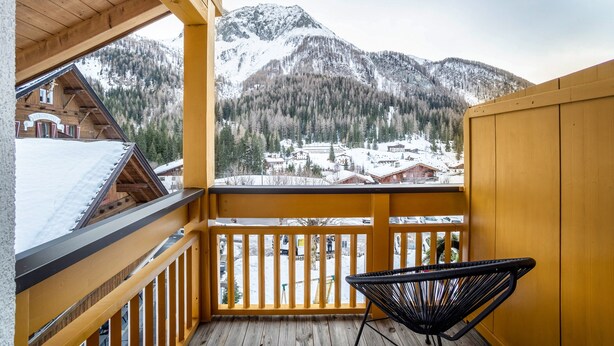 A wooden balcony with a view of snow-covered mountains and a town below. - Apartment "Mountain Residence Kasern Nr 3" with Mountain View, Garden & Wi-Fi (Prettau)