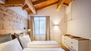 A room with wooden beams, a bed with white bedding, a bedside table with drawers, and a window with curtains. - Apartment "Mountain Residence Kasern Nr 3" with Mountain View, Garden & Wi-Fi (Prettau)
